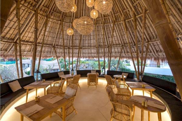 Innenbereich des Eden Beach Khao Lak Resorts & Spa mit runden Tischen und Stühlen unter einem Bambusdach.