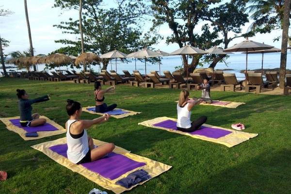 Fünf Personen machen Yoga auf der Wiese am Strand von Khao Lak.