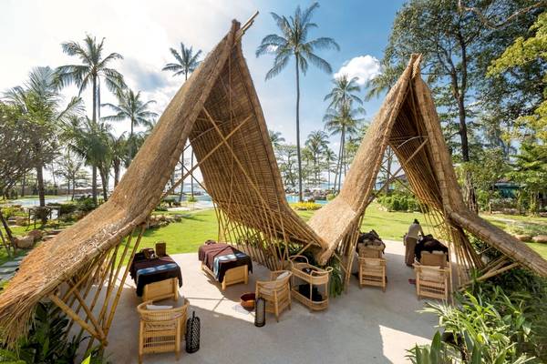 Außenbereich des Eden Beach Khao Lak Resort & Spa mit Bambushütten und Massageliegen.