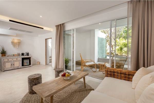 Wohnzimmer im Eden Beach Khao Lak Resort mit Holzmöbeln, einer Couch, einem Tisch und großen Glastüren.