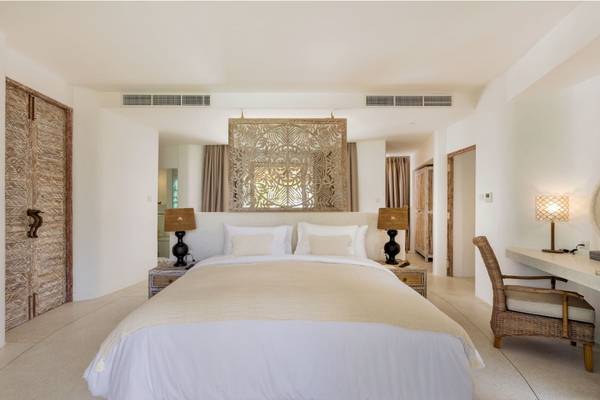 Innenansicht des Schlafzimmers im Eden Beach Khao Lak Resort & Spa mit weißem Bett, Lampen und Wanddekoration.