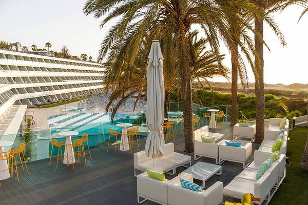 Pool-Terrasse des Santa Monica Suites Hotels mit weißen Möbeln und gelben Stühlen.