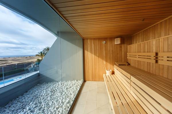 Sauna mit großer Glaswand und Blick auf den Ozean, weiße Kieselsteine auf dem Boden, Holzbänke.