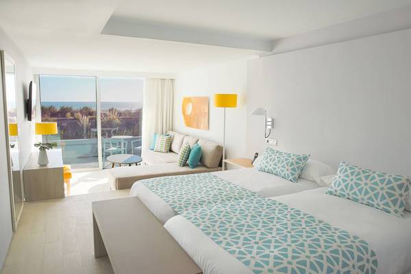 Innenansicht eines Hotelzimmers von Santa Monica Suites mit zwei Betten, Sofa, Tisch, Lampen und Meerblick.