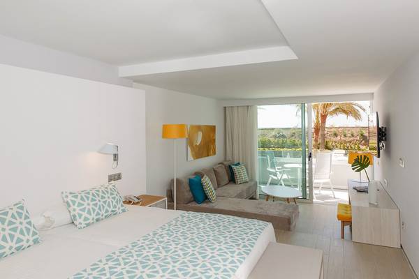 Innenansicht eines Zimmers im Santa Monica Suites Hotel mit einem Bett, einem Sofa, einer Veranda und einer Palme.