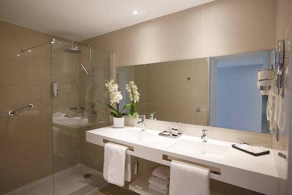 Badezimmer im Santa Monica Suites Hotel mit Glasdusche, Waschbecken und Spiegel.