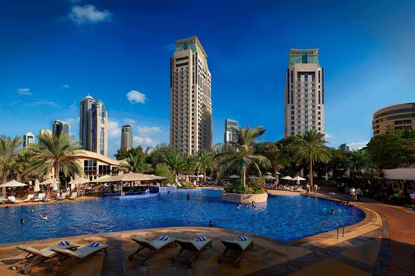 Außenpool des Habtoor Grand Resort & Spa mit vielen Gästen und hohen Gebäuden im Hintergrund.