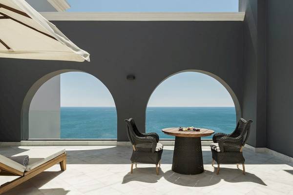 Terrasse mit Meerblick im Mitsis Alila Resort und Spa mit zwei Korbstühlen und einem Tisch.