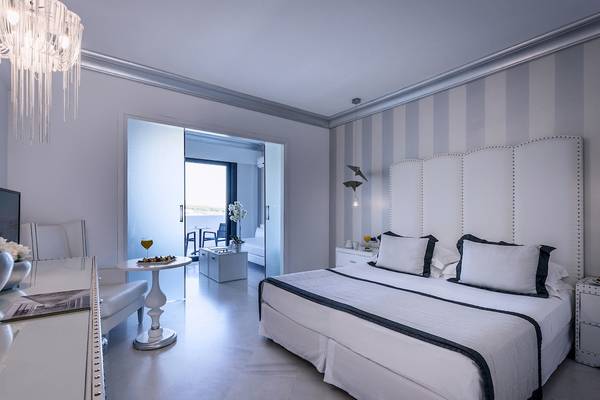 Innenansicht eines Schlafzimmers im Mitsis Alila Resort & Spa mit Bett, Nachttischen und offenem Balkon.