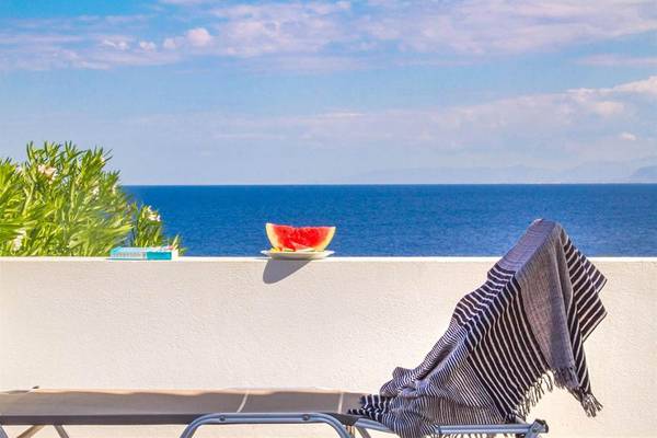 Terrasse mit Meerblick, einer Wassermelone auf einem Teller und einem Liegestuhl.