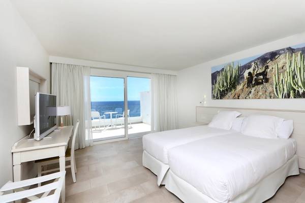 Ein modernes Hotelzimmer mit zwei Betten, Blick auf das Meer und eine Terrasse.