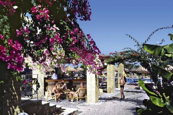 Gäste sitzen draußen an der Bar des Blue Sea Beach Resorts, umgeben von Blumen und Pflanzen.