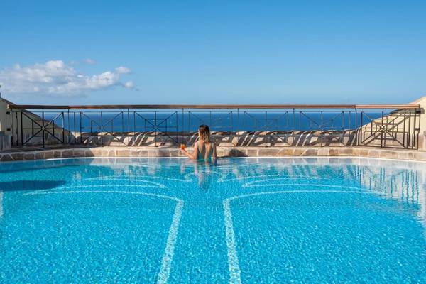 Ein Schwimmbecken mit einer Frau, die auf der Terrasse des GF Gran Costa Adeje mit Blick auf das Meer sitzt.