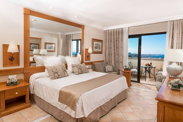 Zimmer im GF Gran Costa Adeje Hotel mit Meerblick, Bett, Möbeln und Balkon.