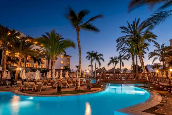 Der Poolbereich des GF Gran Costa Adeje Hotels bei Einbruch der Dunkelheit, mit Palmen und Sonnenliegen.