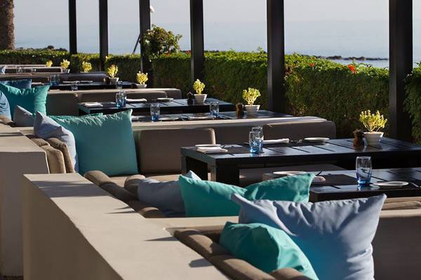 Außensitzbereich im Almyra Hotel mit Tischen und Sofas, Blick aufs Meer.