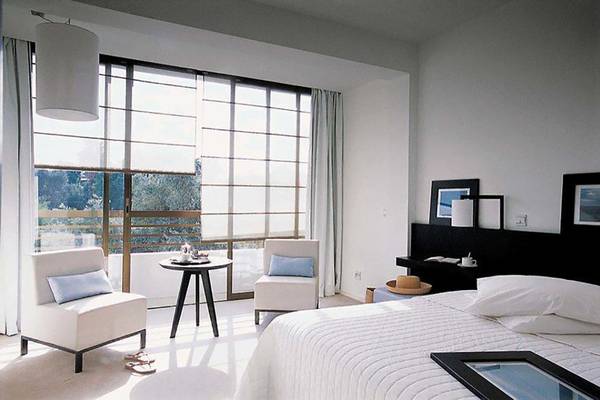 Schlafzimmer im Almyra Hotel mit Bett, zwei Sesseln, Tisch und großem Fenster.