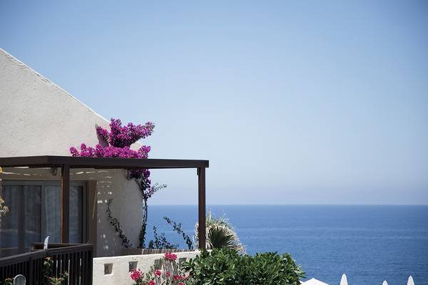 Meerblick von einem Balkon im Sea Side Resort & Spa mit violetten Blumen und einer schattenspendenden Pergola.