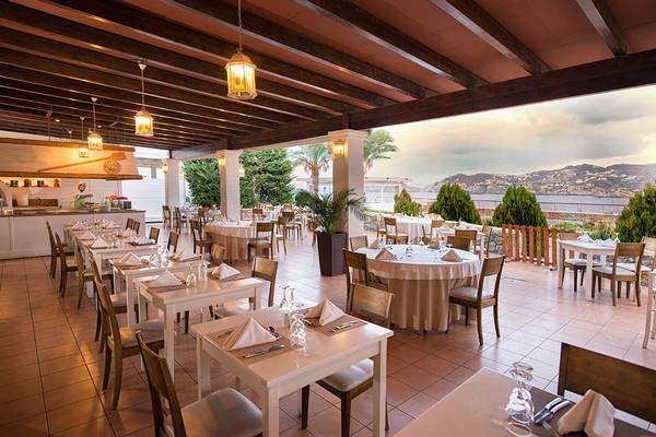 Innenansicht des Restaurants im Sea Side Resort & Spa mit Tischen und Stühlen, Blick auf die Berge und das Meer.