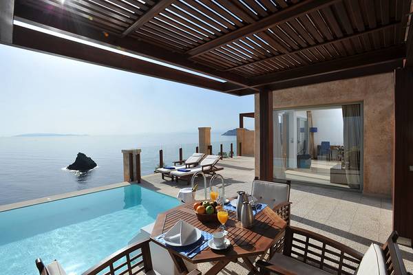 Terrasse des Sea Side Resort & Spa mit Pool und Meerblick, Loungemöbeln und Frühstückstisch.