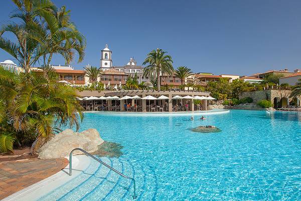Außenpool des Lopesan Villa del Conde Resort & Thalasso mit Palmen und Gebäuden im Hintergrund.