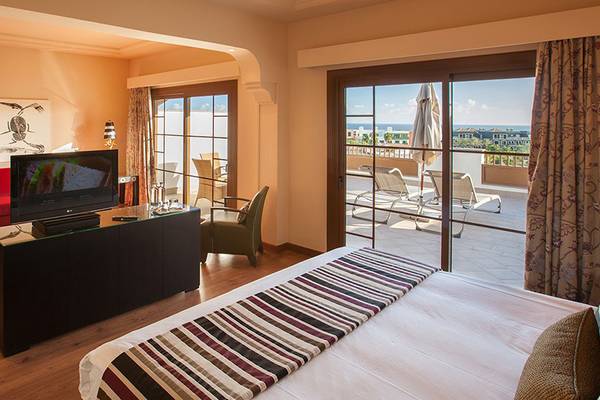 Suite im Lopesan Villa del Conde Resort & Thalasso mit Fernseher, rotem Sessel und Terrassenzugang.