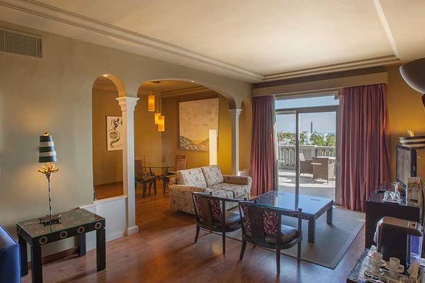Wohnzimmer im Lopesan Villa del Conde Resort & Thalasso mit moderner Einrichtung, Sofa, Tisch, Lampe und Panoramafenster.