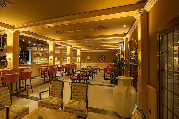 Innenansicht der Bar im Lopesan Villa del Conde Resort & Thalasso Hotel mit Holztheke, roten Stühlen und Tischen.