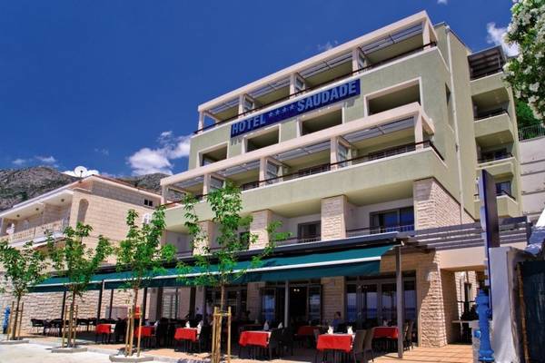 Außenansicht des Saudade Hotels mit grüner Markise und roten Tischen vor dem Gebäude.