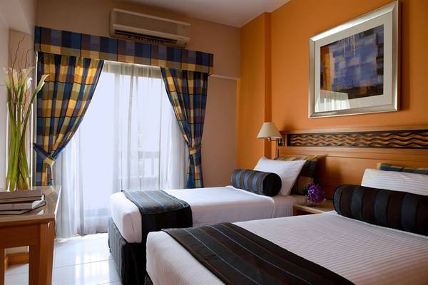 Zwei Betten im Zimmer des Golden Sands Hotel Apartments mit oranger Wand und gemusterten Vorhängen.