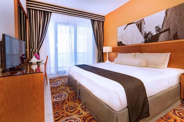 Schlafzimmer im Golden Sands Hotel Apartments mit Doppelbett, Fernseher, Nachttisch und Fenstern.