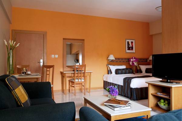 Zimmer im Golden Sands Hotel Apartments mit Bett, Tisch, Stuhl, Fernseher und Dekor.
