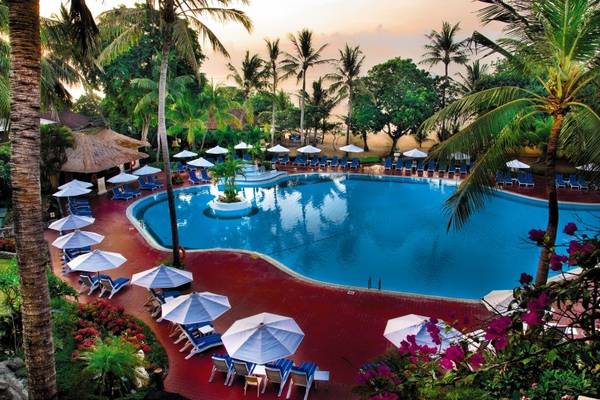 Außenansicht des Swimmingpools im Prama Sanur Beach Bali Hotel mit Sonnenliegen und Schirmen.