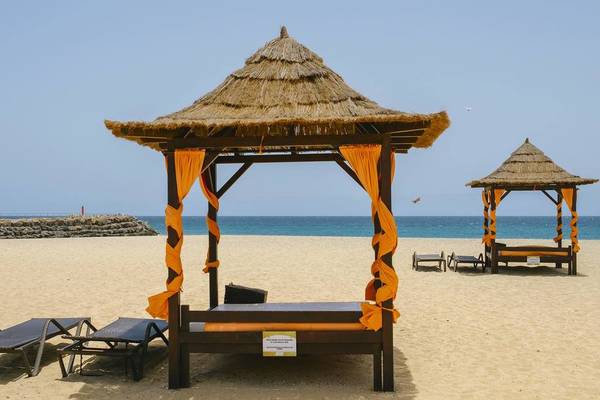 Zwei Sonnenbetten am Strand des Melia Dunas Beach Resort & Spa mit orangefarbenen Vorhängen.