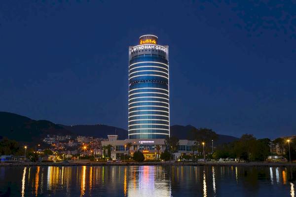 Wyndham Grand Izmir Ozdilek Hotel bei Nacht, beleuchtet mit Lichtern, am Ufer gelegen.