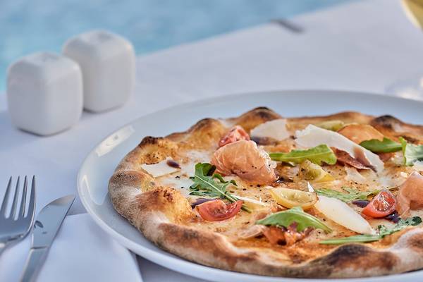 Eine frisch zubereitete Pizza mit Tomaten, Käse und anderen Zutaten auf einem weißen Teller.