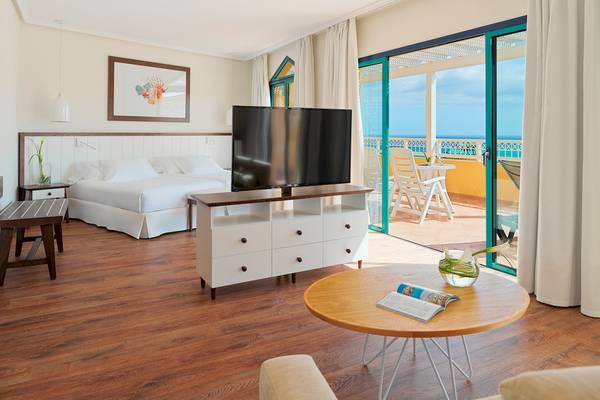 Innenansicht eines Zimmers im H10 Playa Esmeralda Hotel mit Bett, Fernseher und Balkon.