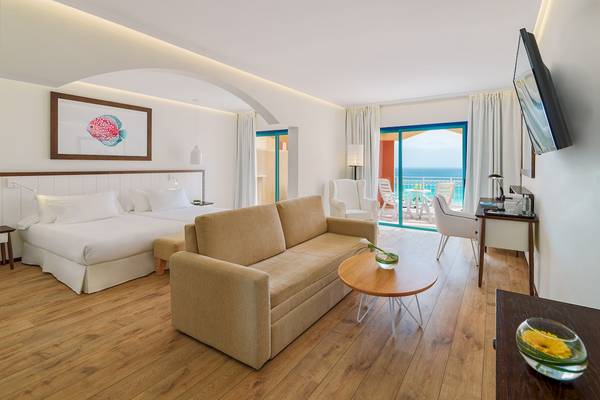 Hotelzimmer des H10 Playa Esmeralda mit Doppelbett, Couch, Tisch, Fernseher und Meerblick.