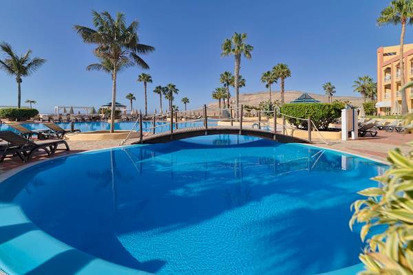 Ein Swimmingpool im Hotel H10 Playa Esmeralda mit einer Brücke und Sonnenliegen in der Umgebung.