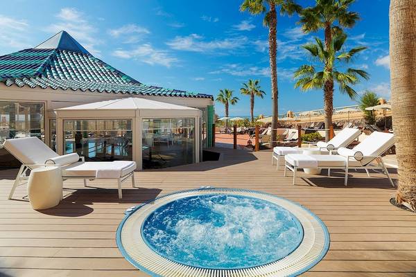Terrasse des H10 Playa Esmeralda Hotels mit Whirlpool und weißen Liegen unter Palmen