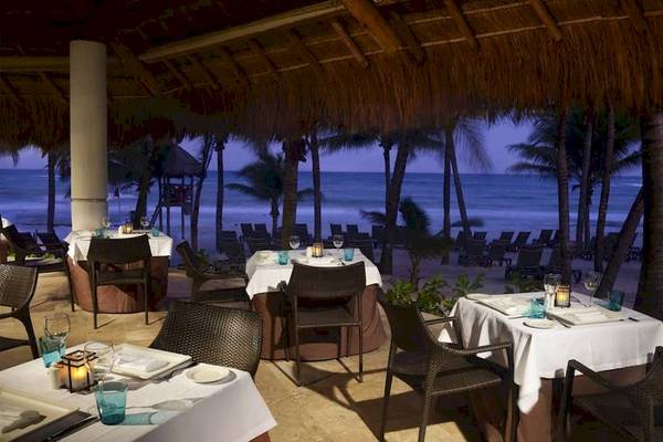 Außenbereich des Catalonia Royal Tulum Hotels mit Tischen und Stühlen, die Meerblick bieten.
