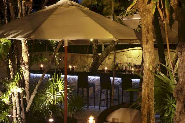 Beleuchtete Hotelbar im Freien des Catalonia Royal Tulum, mit einem großen Schirm und leuchtenden Tischen.