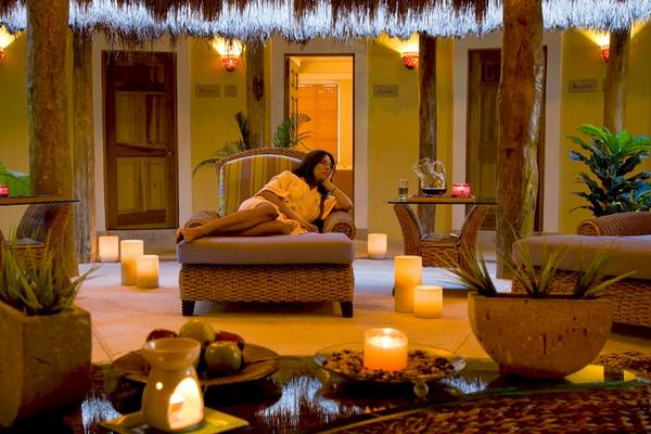 Eine Frau entspannt sich im Wellnessbereich des Hotels Catalonia Royal Tulum, umgeben von Kerzen und Pflanzen.