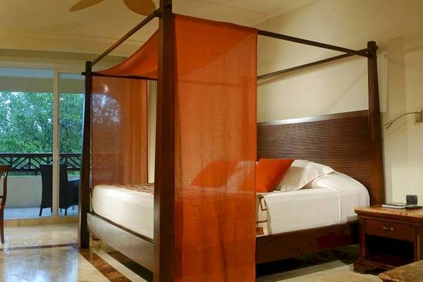 Ein Hotelzimmer mit einem Baldachin-Bett, weißem Bettlaken, orangefarbenen Kissen und einem Schreibtisch.