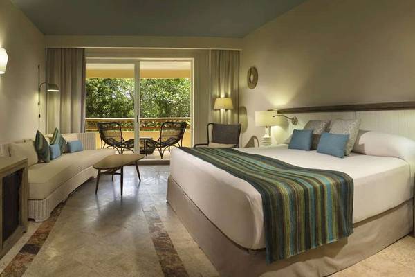 Ein modernes Hotelzimmer im Catalonia Royal Tulum mit einem großen Bett, einem Sofa und einem Balkon mit Möbeln.