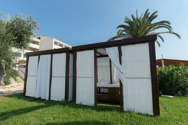Schlafzelt im Garten des Elea Beach Hotels mit weißem Vorhang und Palme im Hintergrund.