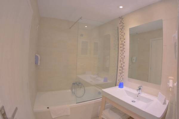 Badezimmer im Elea Beach Hotel mit Badewanne, Dusche, Waschbecken und Spiegel.