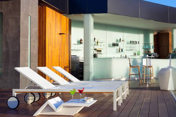 Lounge-Terrasse des Tigotan Lovers & Friends Hotels mit weißen Liegen und einer Bar.