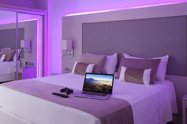 Hotelzimmer mit Laptop auf dem Bett und violetten Lichtern an der Wand.