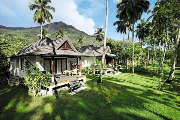 Außenansicht des Hilton Seychelles Labriz Resort & Spa mit zwei Chalets, umgeben von Palmen und grüner Landschaft.